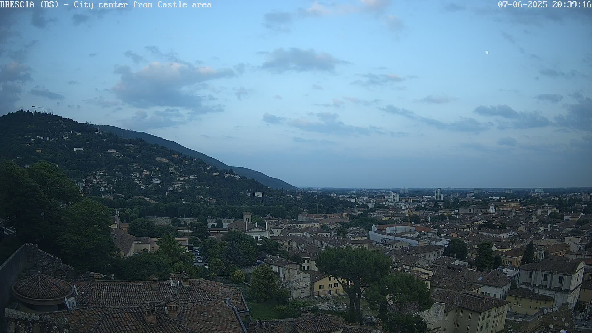 An expansive view of a city nestled against a hill, under a twilight sky with a few clouds.