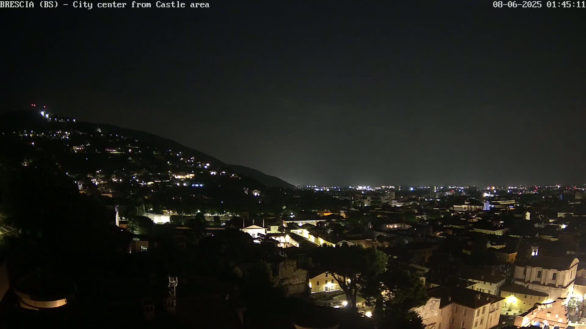 A nighttime view of a city nestled against a hill, with numerous lights illuminating buildings and streets under a dark sky.