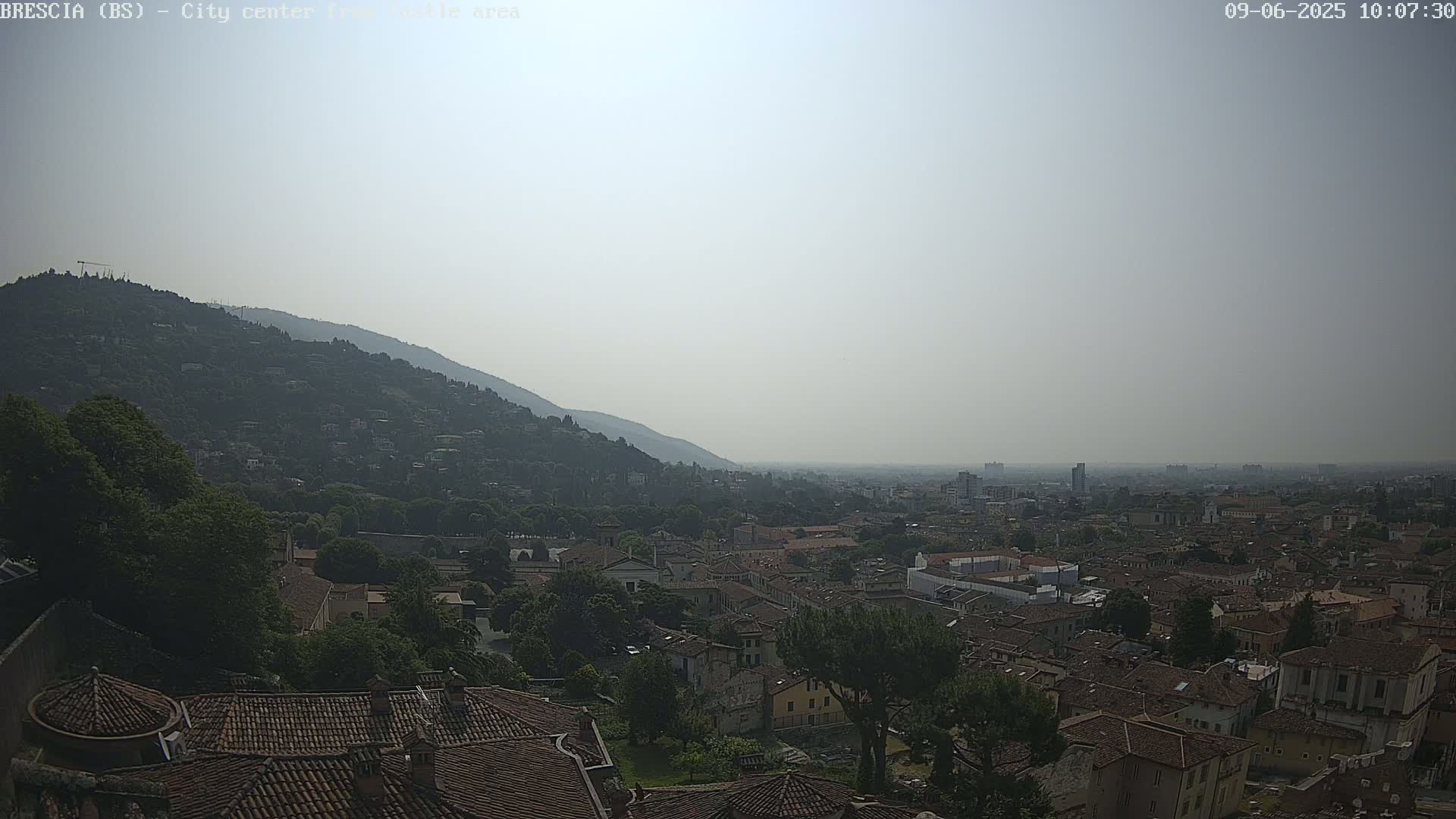 A hazy, sunny day overlooks a sprawling city nestled against a tree-covered mountain.