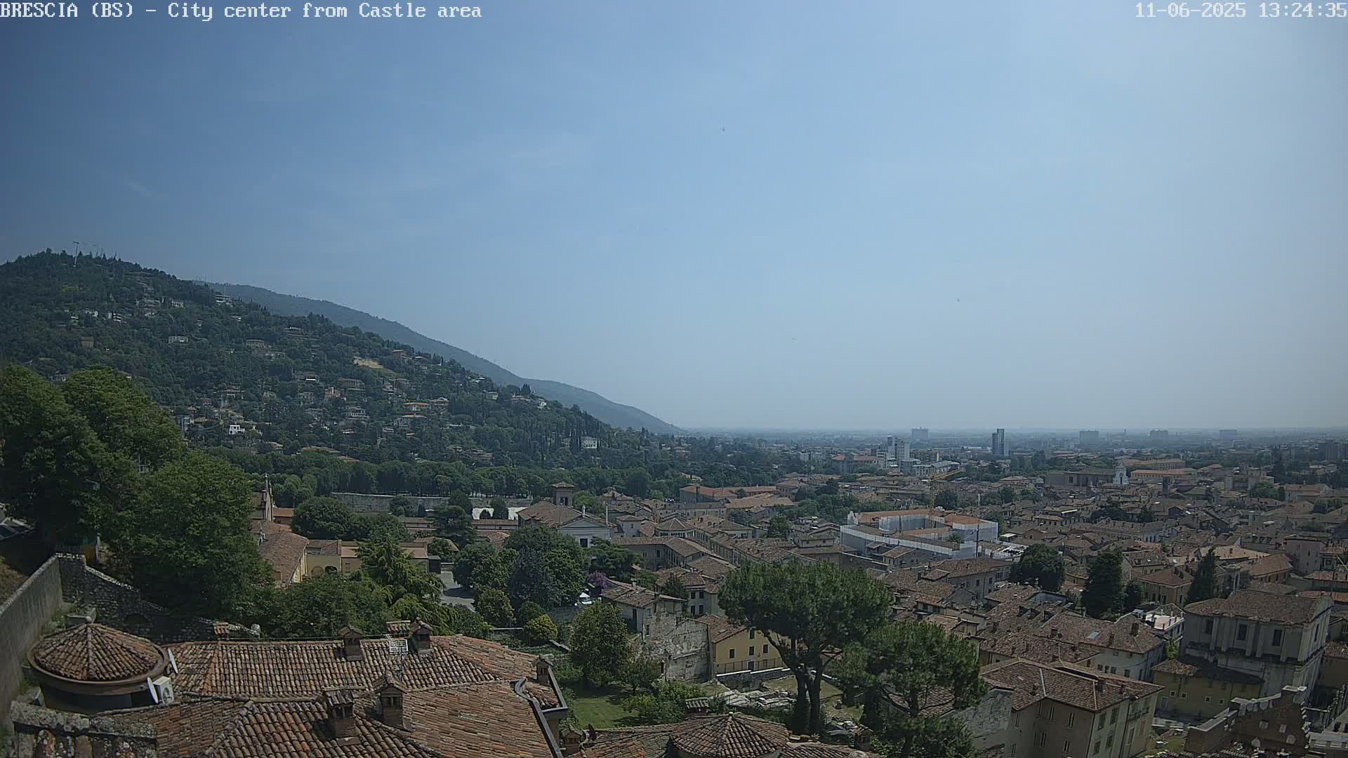 A sprawling city with terracotta rooftops nestled against a verdant hillside under a clear, bright sky.