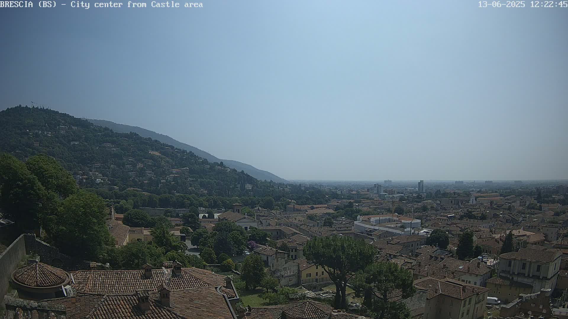 A hazy, sunny day reveals a sprawling city nestled in a valley, bordered by a verdant hillside.