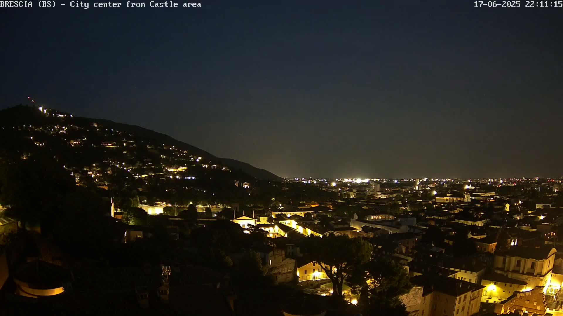 A nighttime view of a city nestled against a hill, illuminated by numerous lights under a clear, dark sky.
