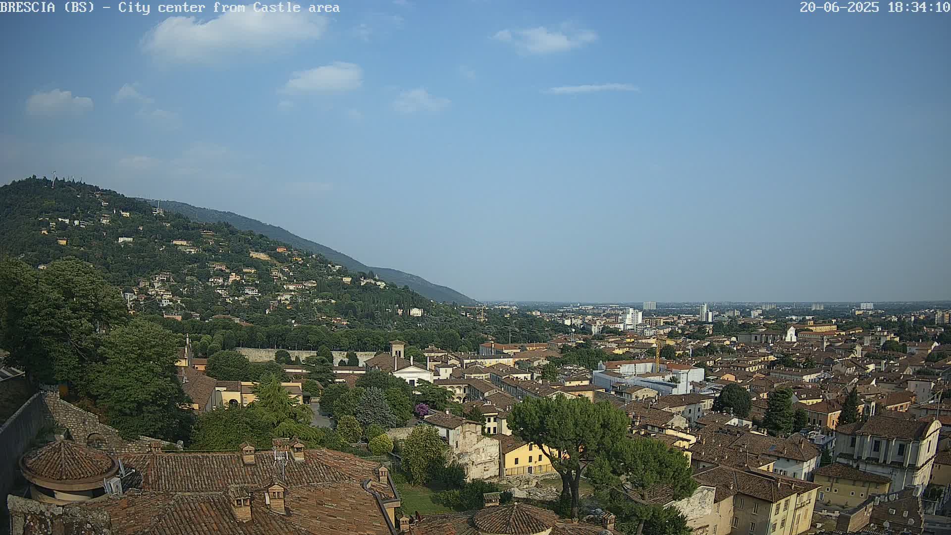 A sprawling city nestled against a hillside under a mostly clear, sunny sky.