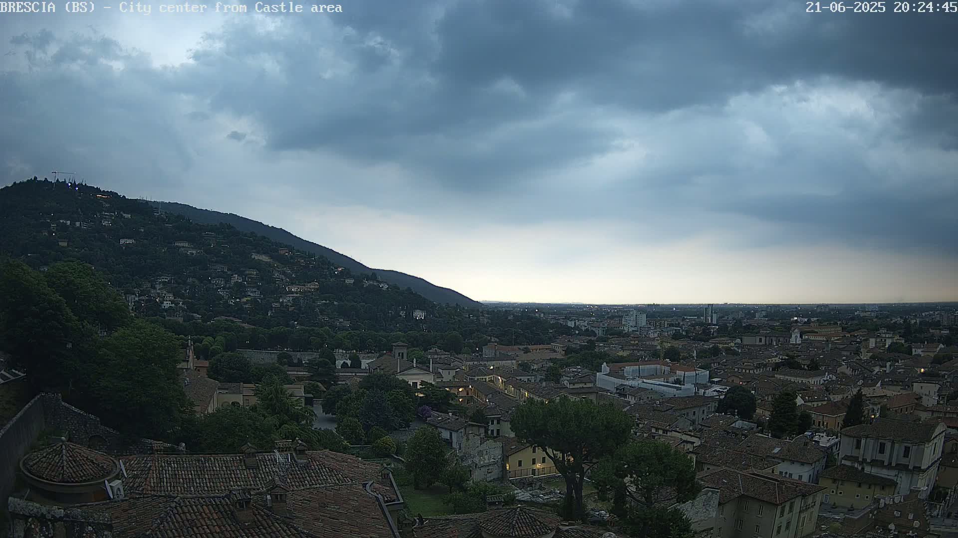 An expansive view of a city nestled at the base of a hill under a cloudy, dusky sky.