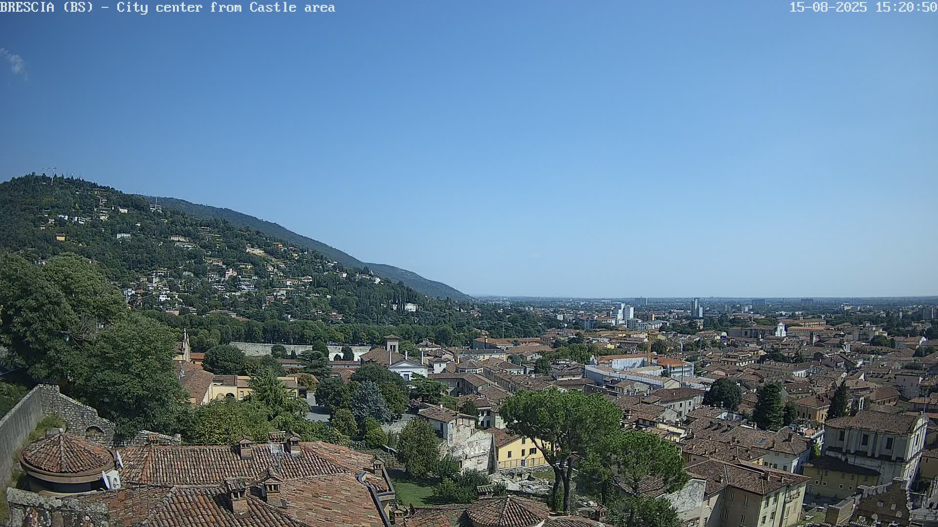 A sunny day reveals a panoramic view of a city nestled below a hill, with a hazy plain extending beyond.