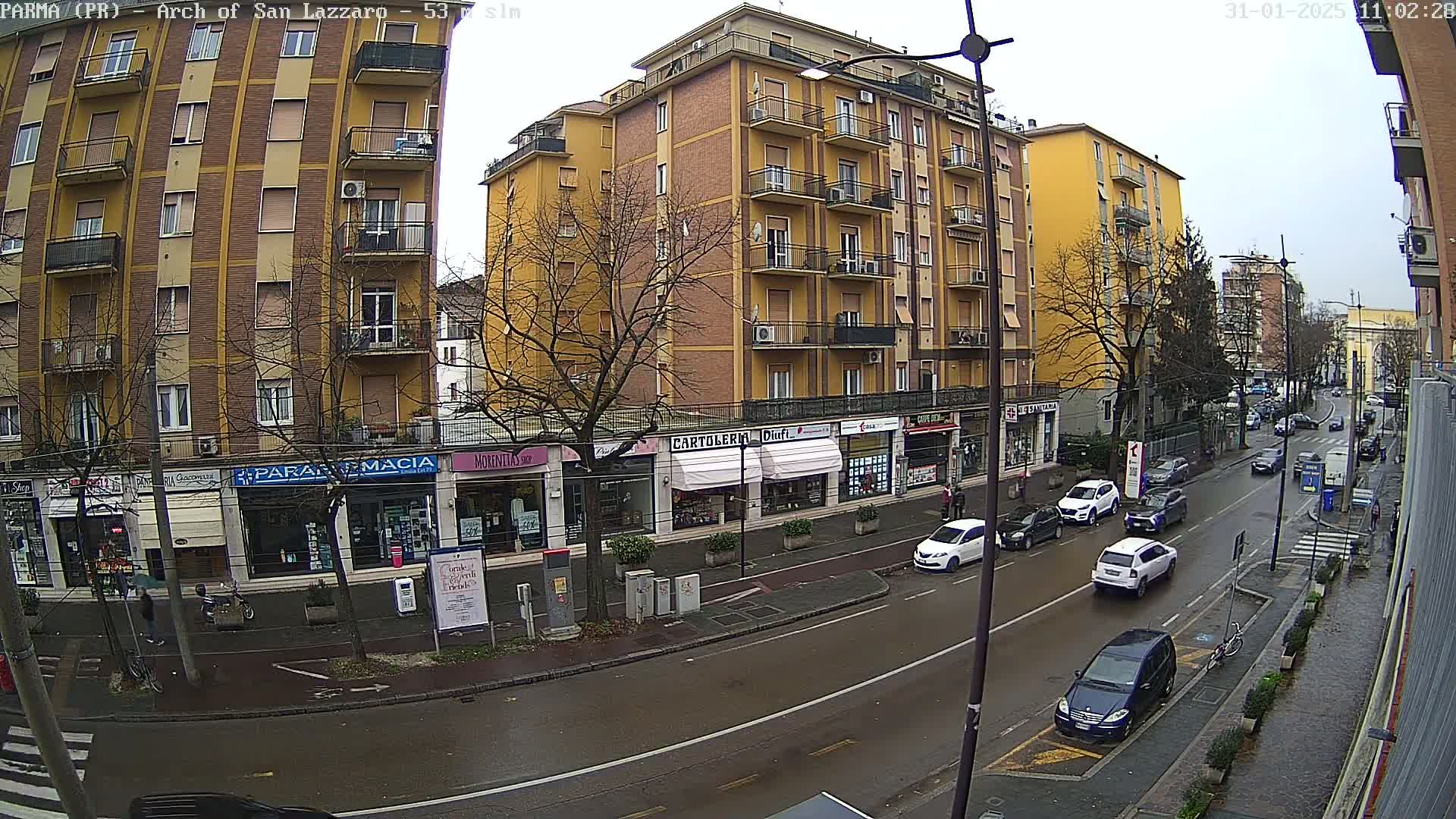 A wet city street lined with shops and a multi-story building under an overcast sky.