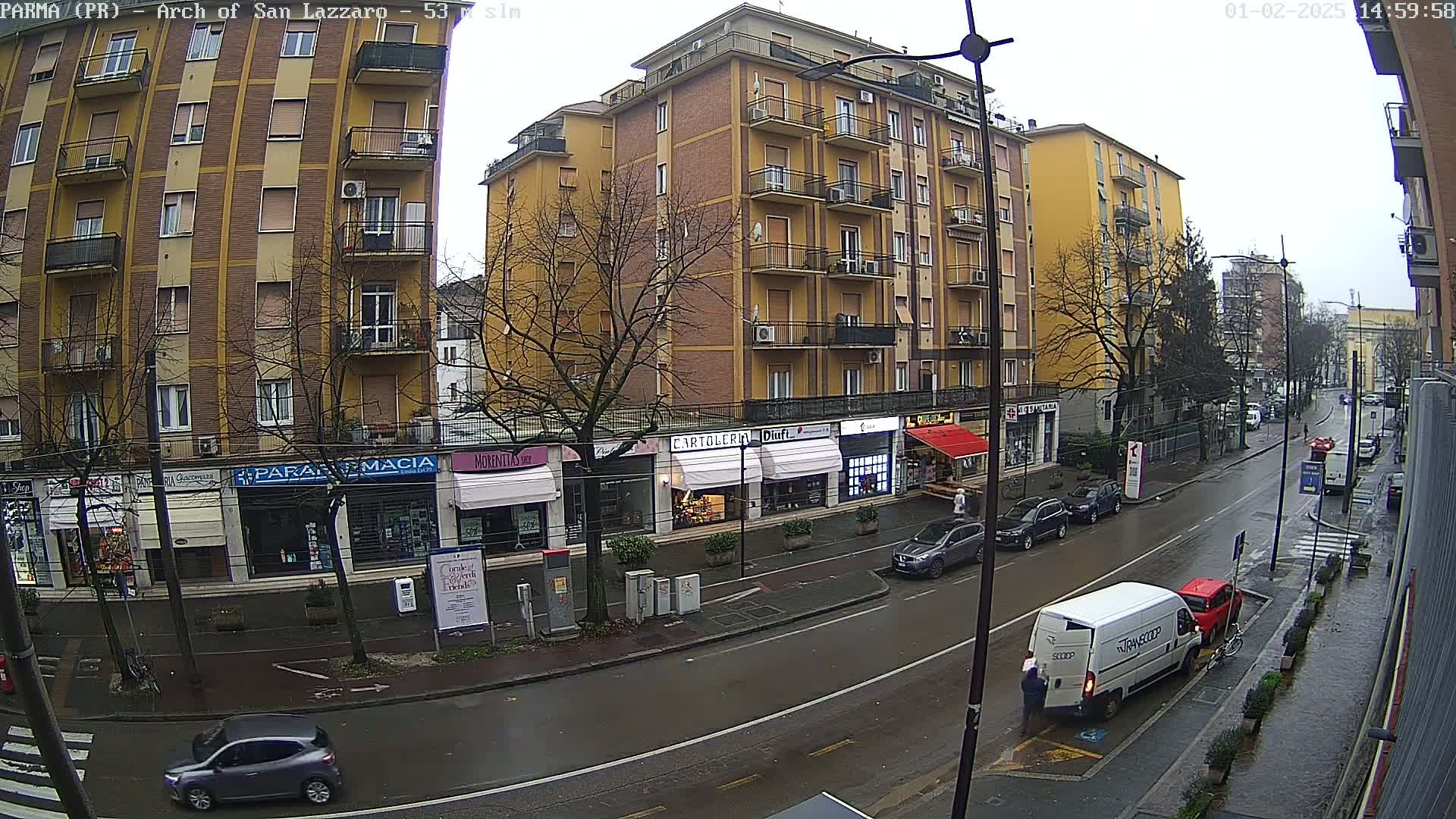 A rain-slicked street scene shows several cars parked along the curb in front of multi-story buildings, with a delivery van stopped in the road.