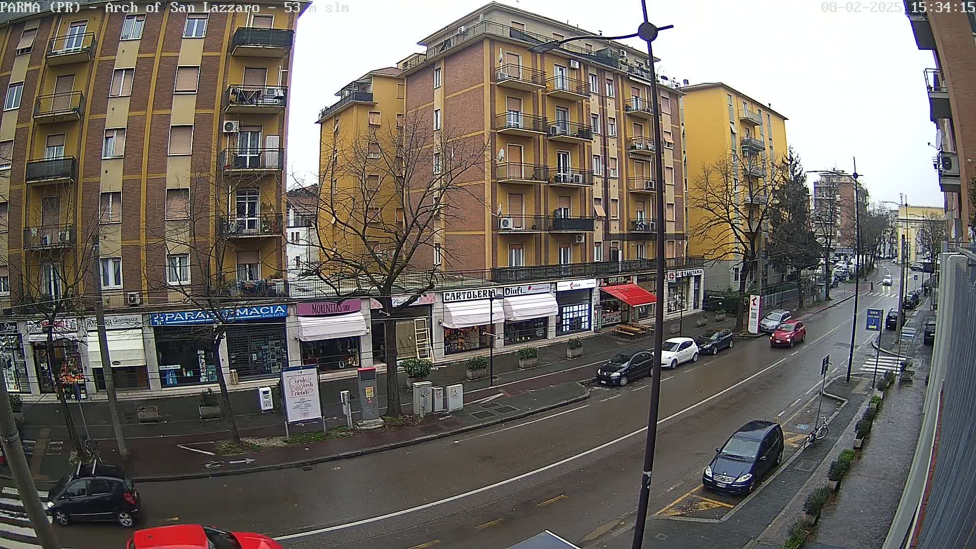 A wet city street lined with multi-story buildings and shops on an overcast day.