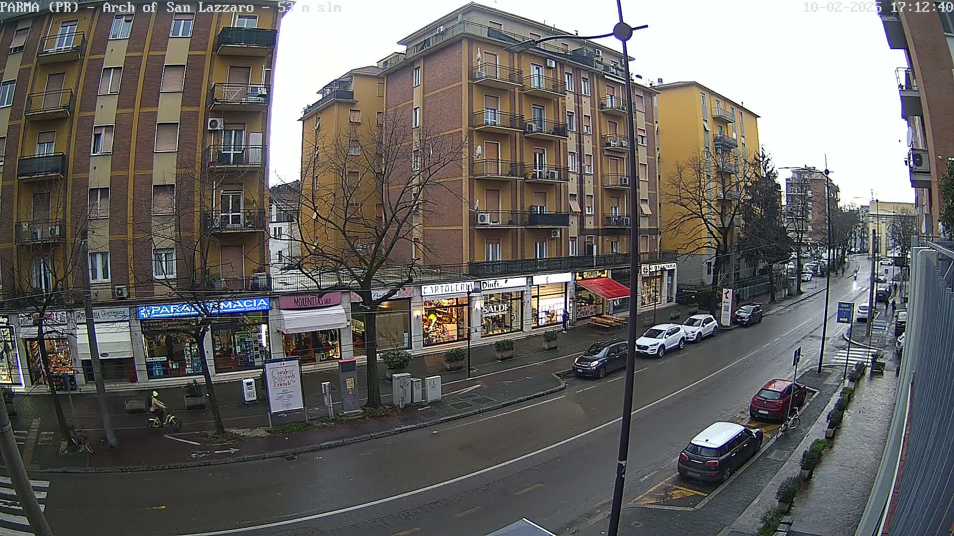 A wet city street lined with multi-story buildings and shops, under an overcast sky.