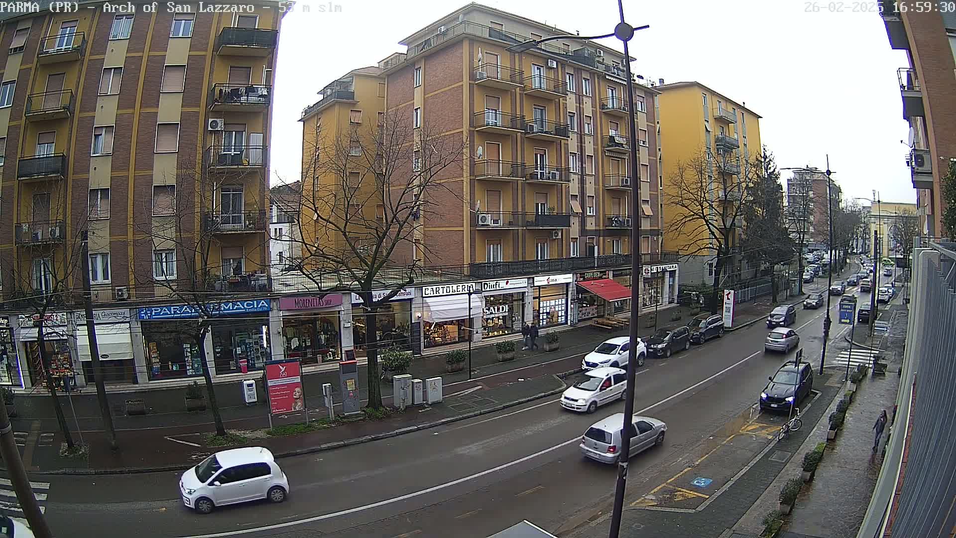A city street scene on an overcast day shows several multi-story buildings and numerous cars driving along a multi-lane road.