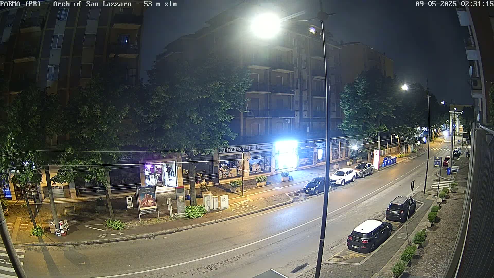 A nighttime street scene shows a multi-story building and several parked cars under bright streetlights.