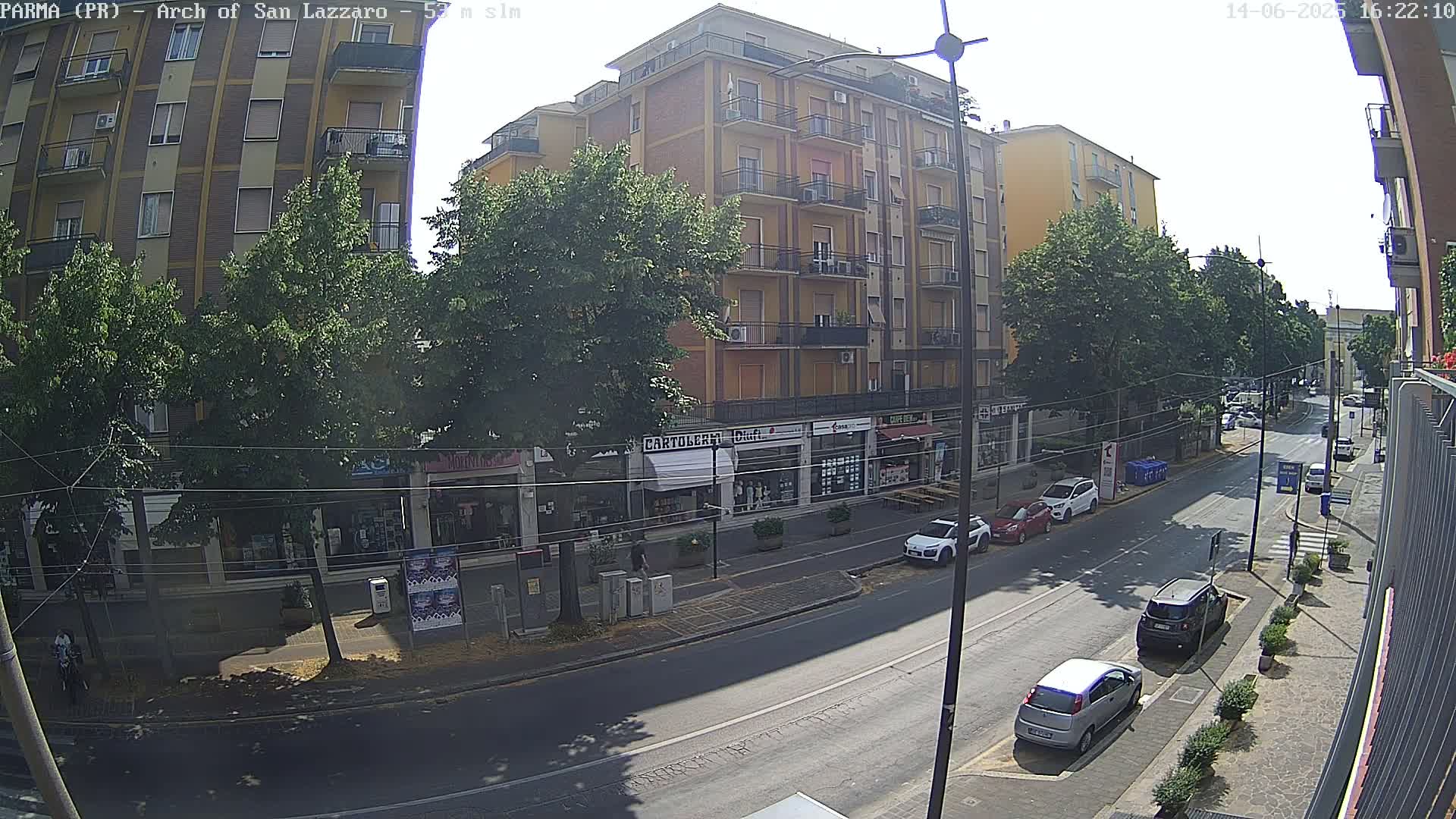 A sunny day reveals a city street lined with multi-story buildings and parked cars, under a clear sky.