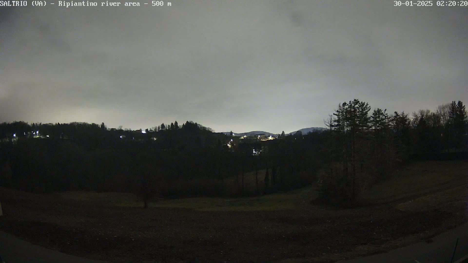 A nighttime view of a dark, treelined hillside under a cloudy sky.