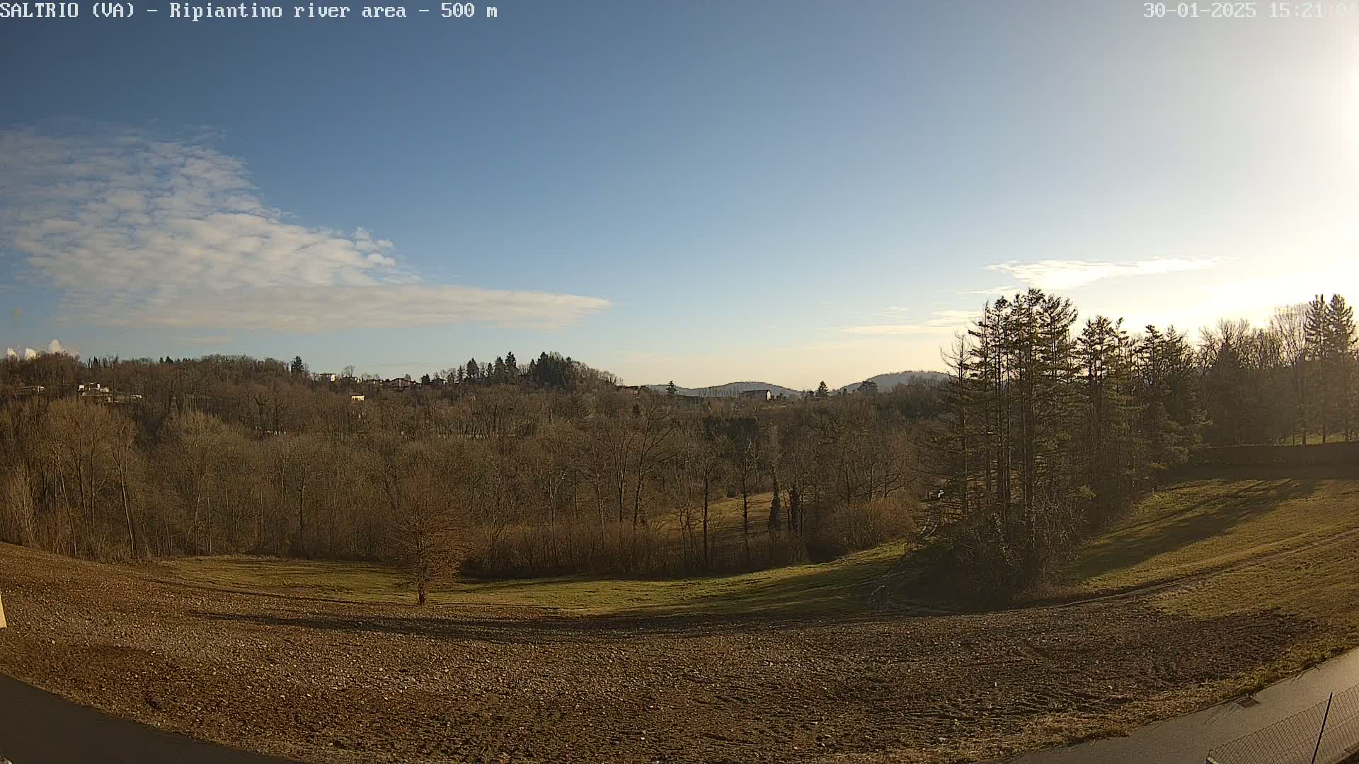 A mostly clear blue sky over a rural landscape of bare winter trees, plowed fields, and distant hills.
