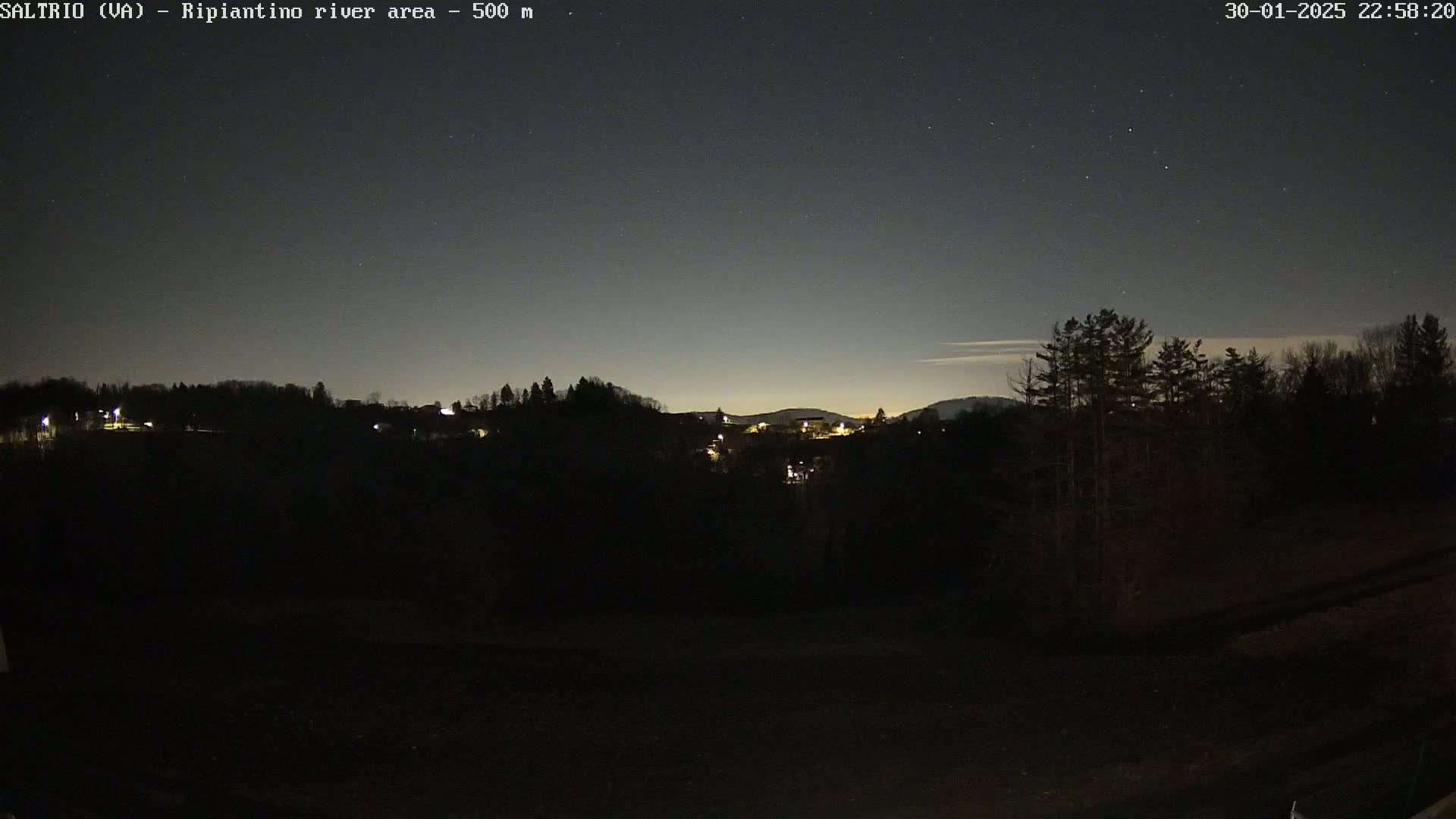 A nighttime view of a dark, silhouetted landscape with a few distant lights, under a clear, starry sky.