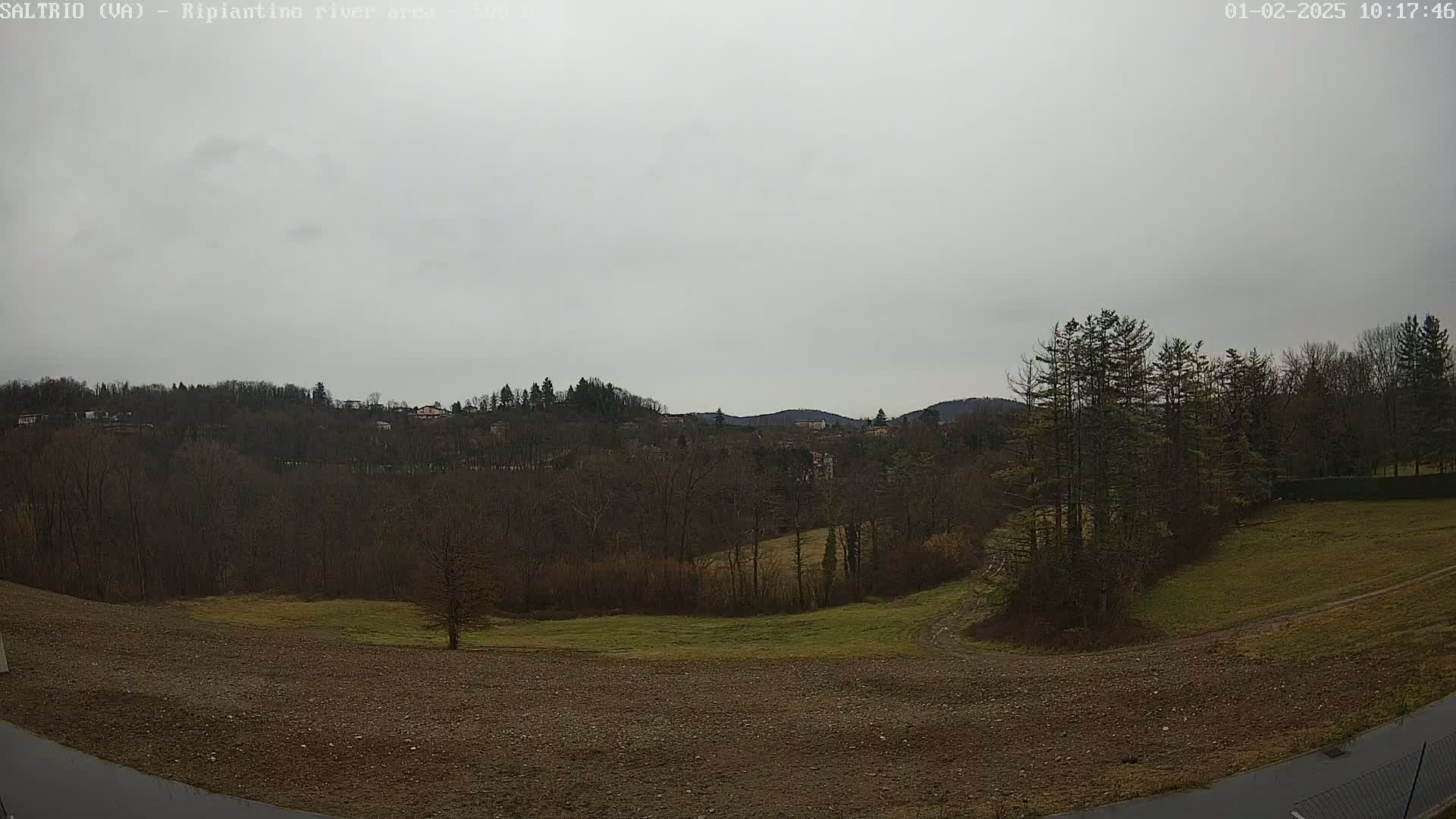 A view of a hilly landscape with bare trees under an overcast sky shows a mix of plowed and grassy fields in the foreground.