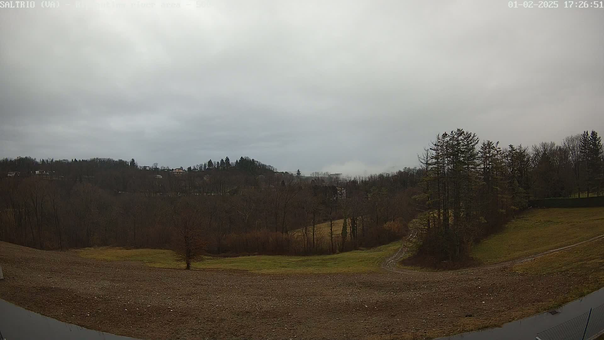 A view of a hilly landscape under an overcast sky shows bare, deciduous trees and patches of grass, with a plowed field in the foreground.