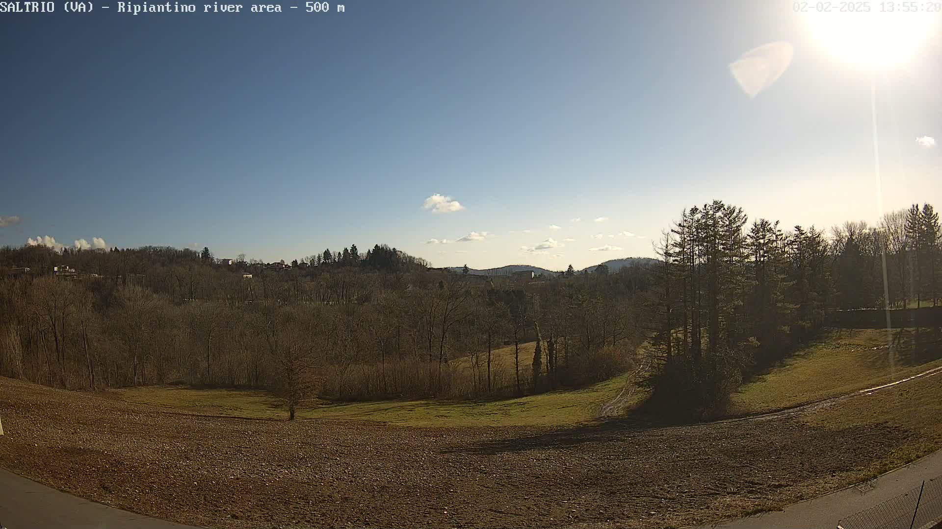 A mostly sunny day reveals a view of a plowed field, bare winter trees, and distant hills under a clear blue sky.