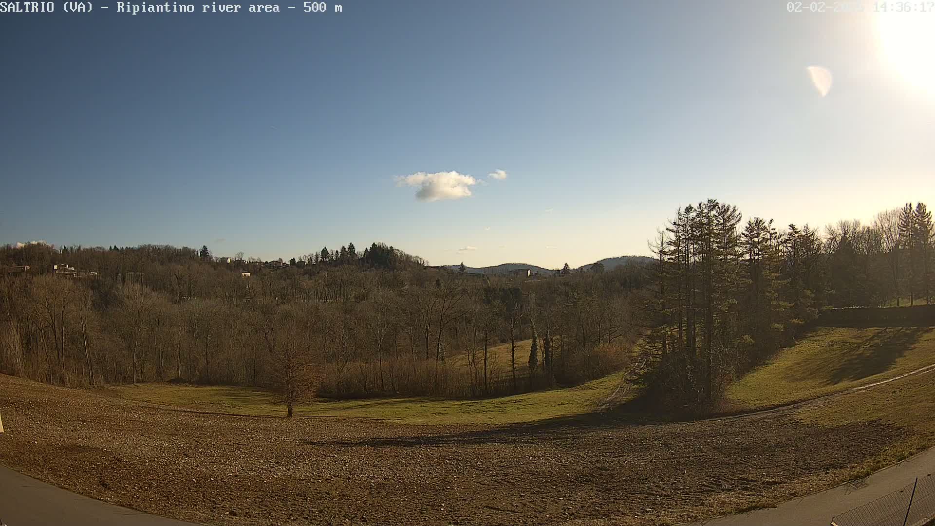 A mostly sunny, clear day reveals a view of a plowed field, grassy areas, and a background of leafless trees and hills.