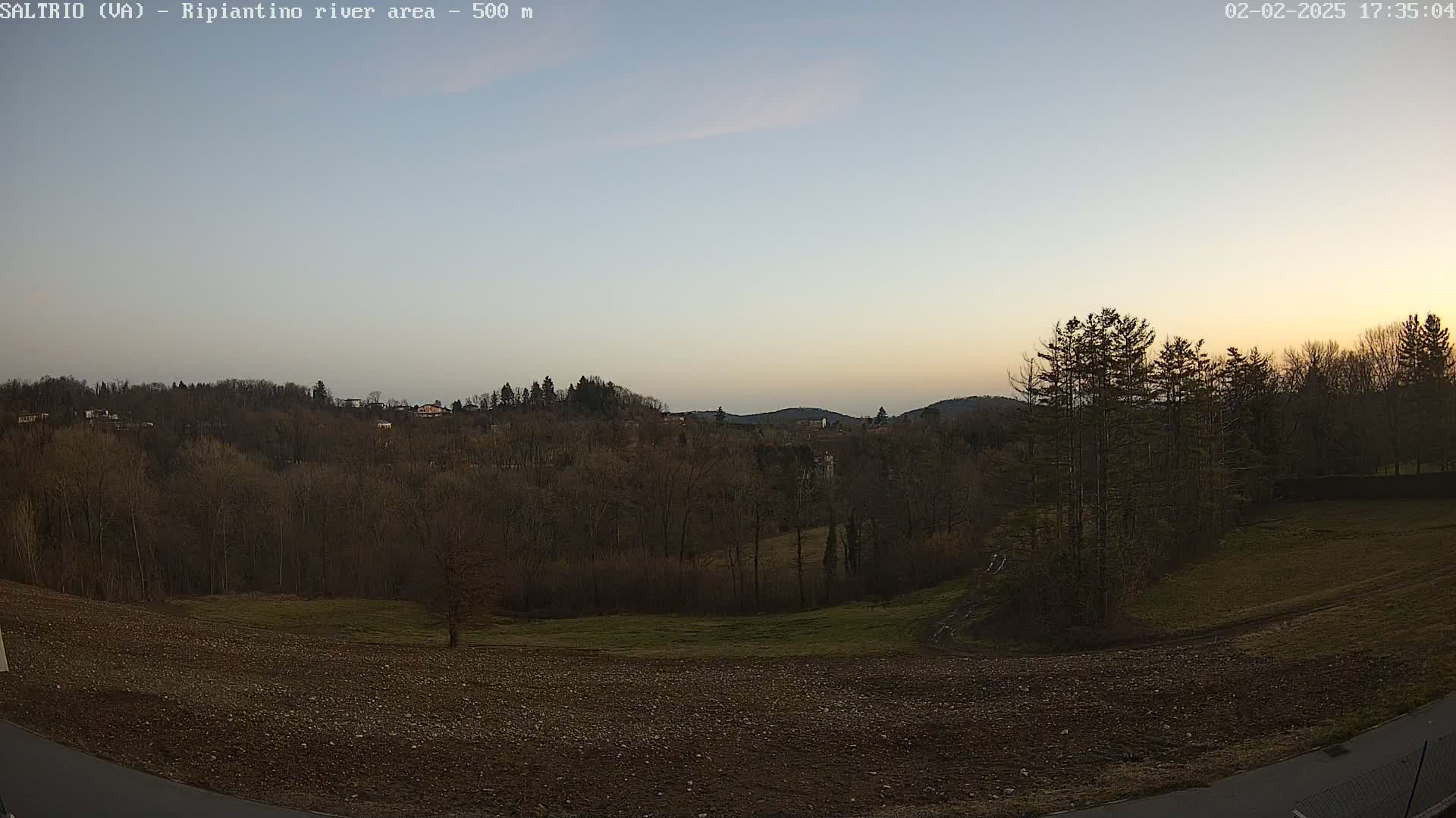 A mostly clear twilight sky overlooks a sparsely wooded area with a plowed field in the foreground.