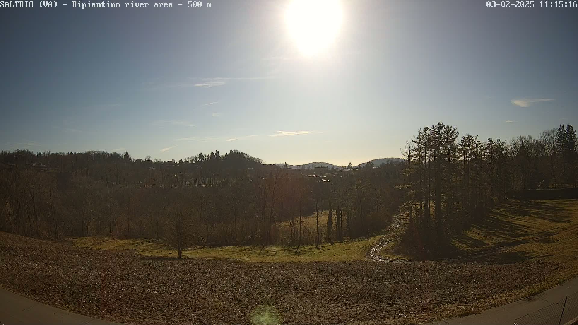 A sunny day reveals a plowed field, sparsely treed areas, and a distant town nestled among hills.