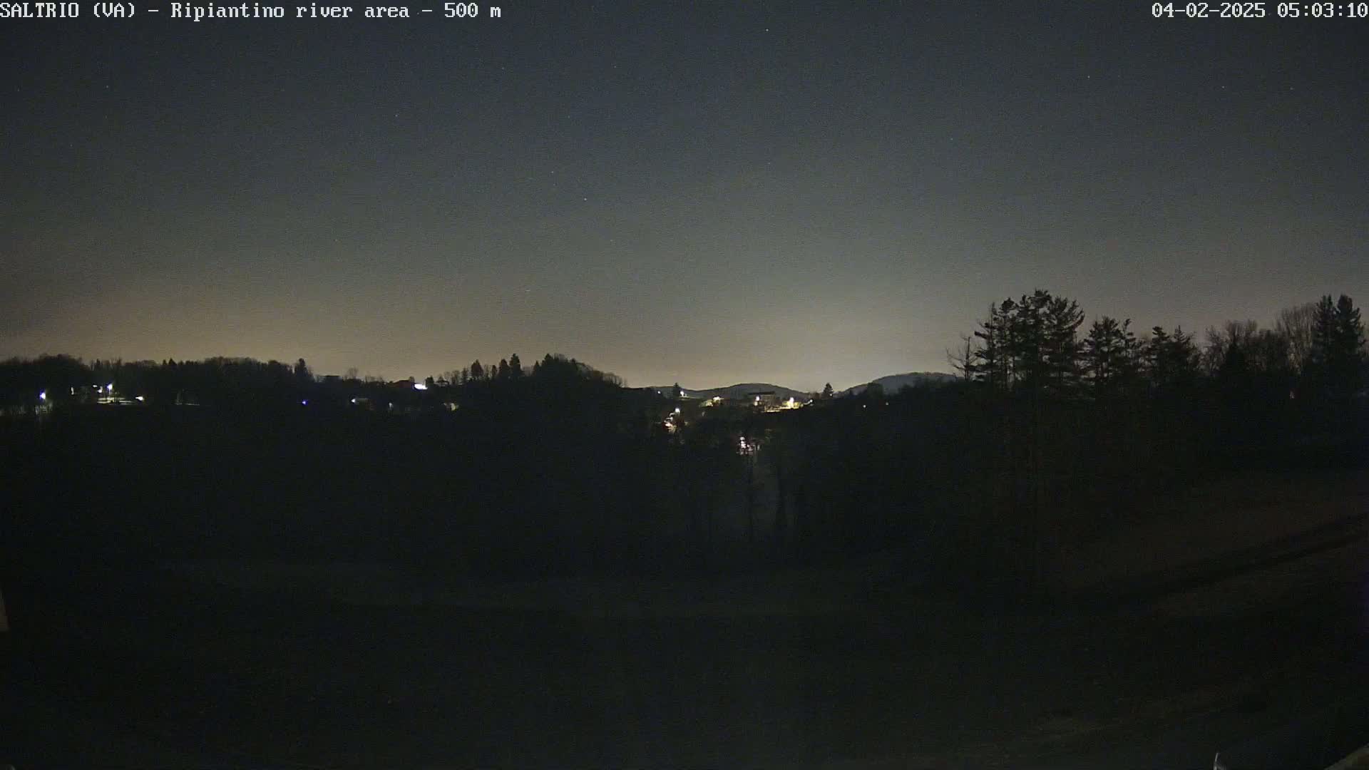 A nighttime view of a dark, silhouetted landscape with a few distant lights and a mostly clear sky.