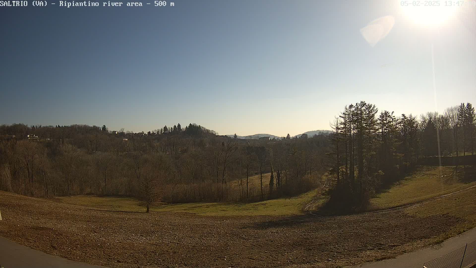 A sunny day reveals a landscape of brown plowed fields, bare winter trees, and distant hills under a clear blue sky.