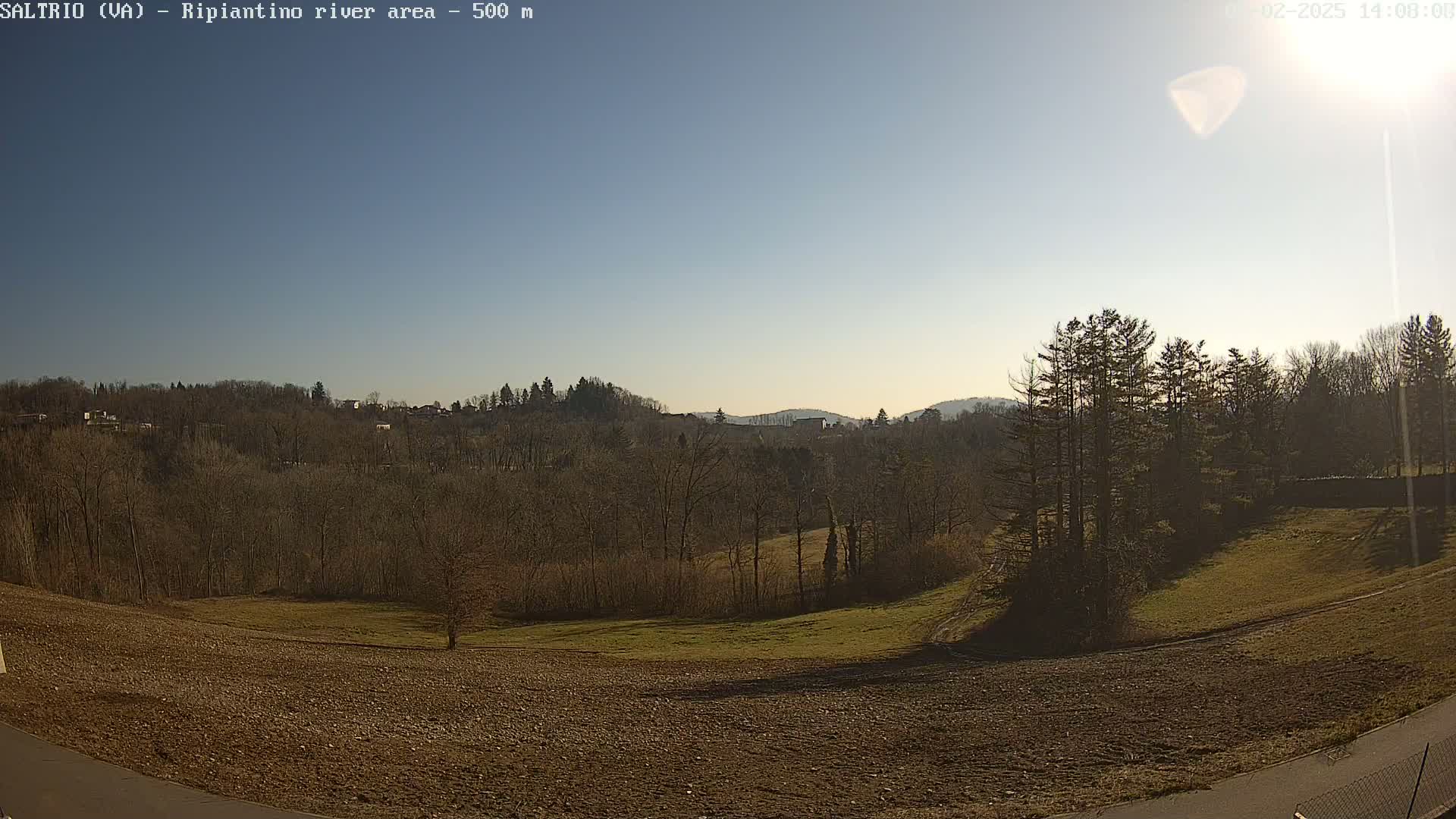 A mostly sunny day reveals a plowed field in the foreground, leading to a line of bare deciduous trees and hills in the background.