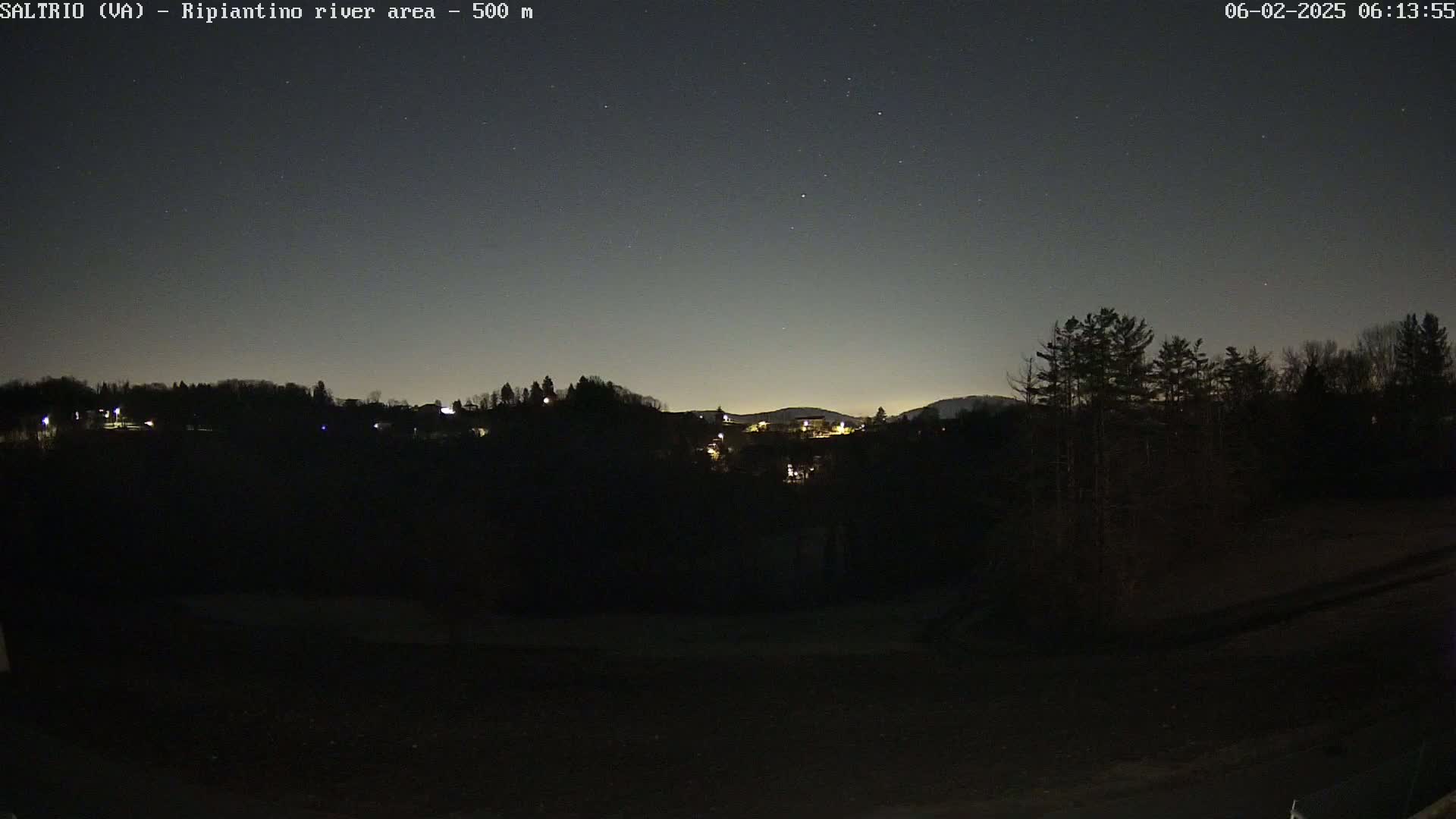 A nighttime view of a dark, hilly landscape with a few scattered lights visible in the distance under a clear, starlit sky.