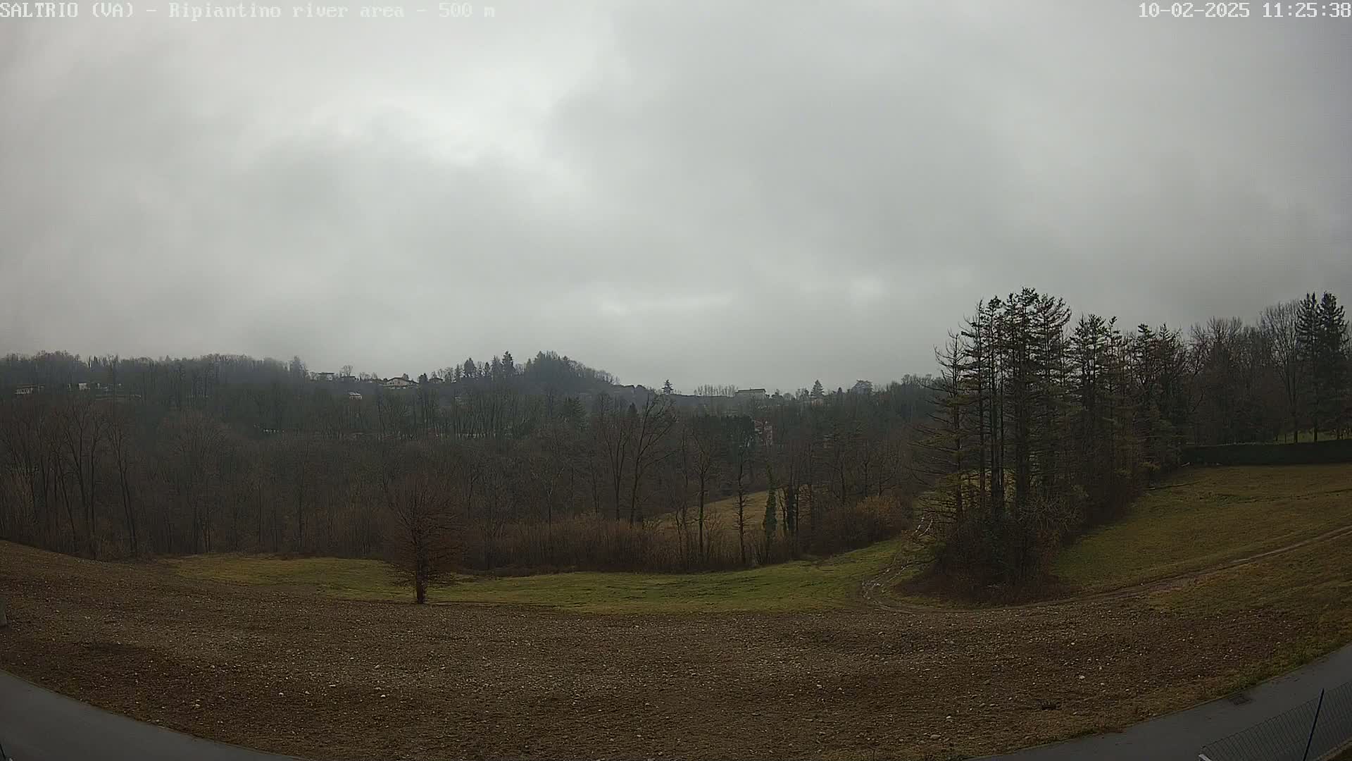 A mostly overcast sky hangs over a rural landscape of bare trees, brown fields, and a few distant houses nestled among the hills.
