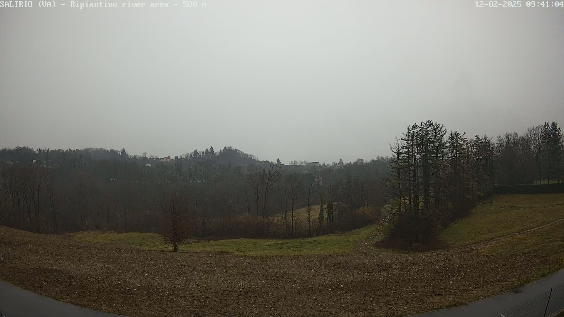 A hazy, overcast day reveals a view of barren, rolling hills and sparsely wooded areas, with a paved road visible in the foreground.