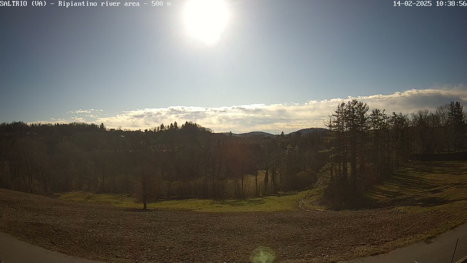 A sunny day with partly cloudy skies over a landscape of plowed fields, bare trees, and distant hills.