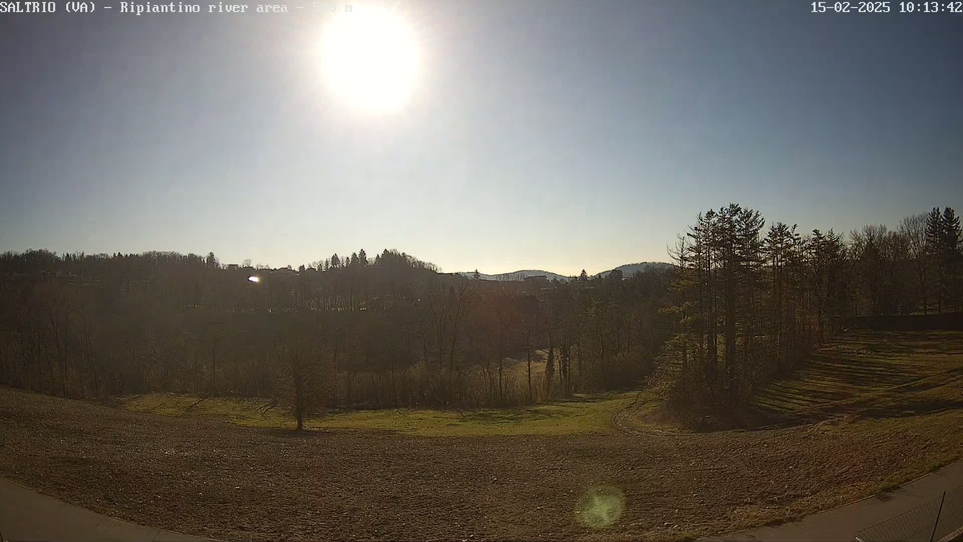 A bright, sunny day reveals a view of plowed fields, a stand of trees, and hills in the distance.