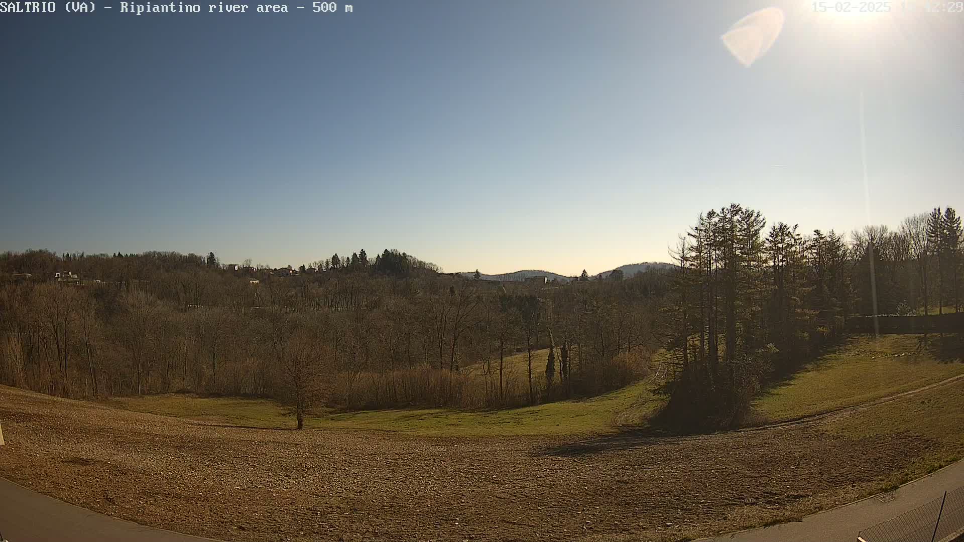 A sunny day reveals a landscape of bare winter trees, fields, and a distant hilltop under a clear blue sky.