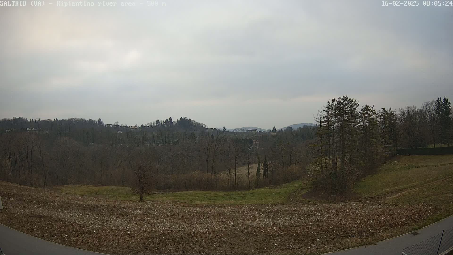 A view of a hilly landscape under an overcast sky, showing bare trees and a plowed field in the foreground.