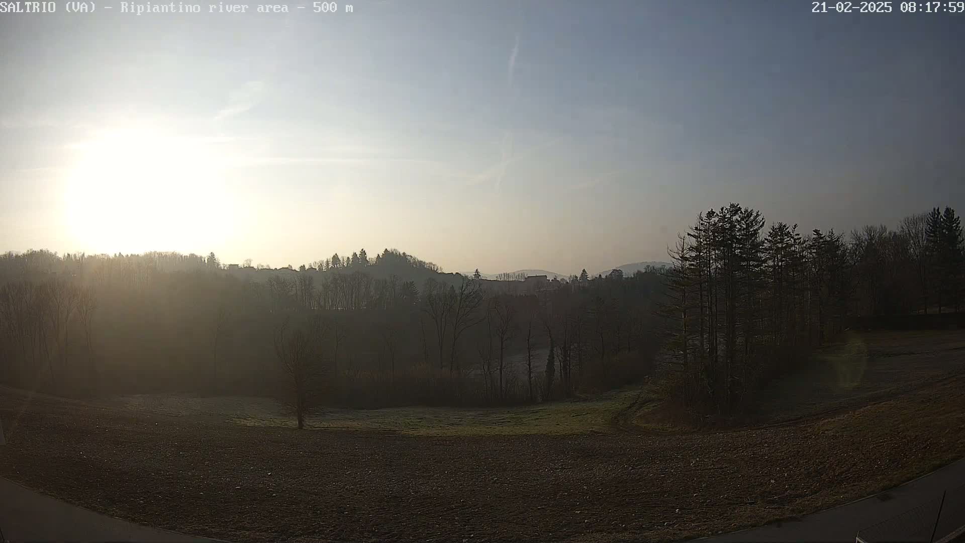 A hazy sunrise illuminates a plowed field and tree-covered hills.