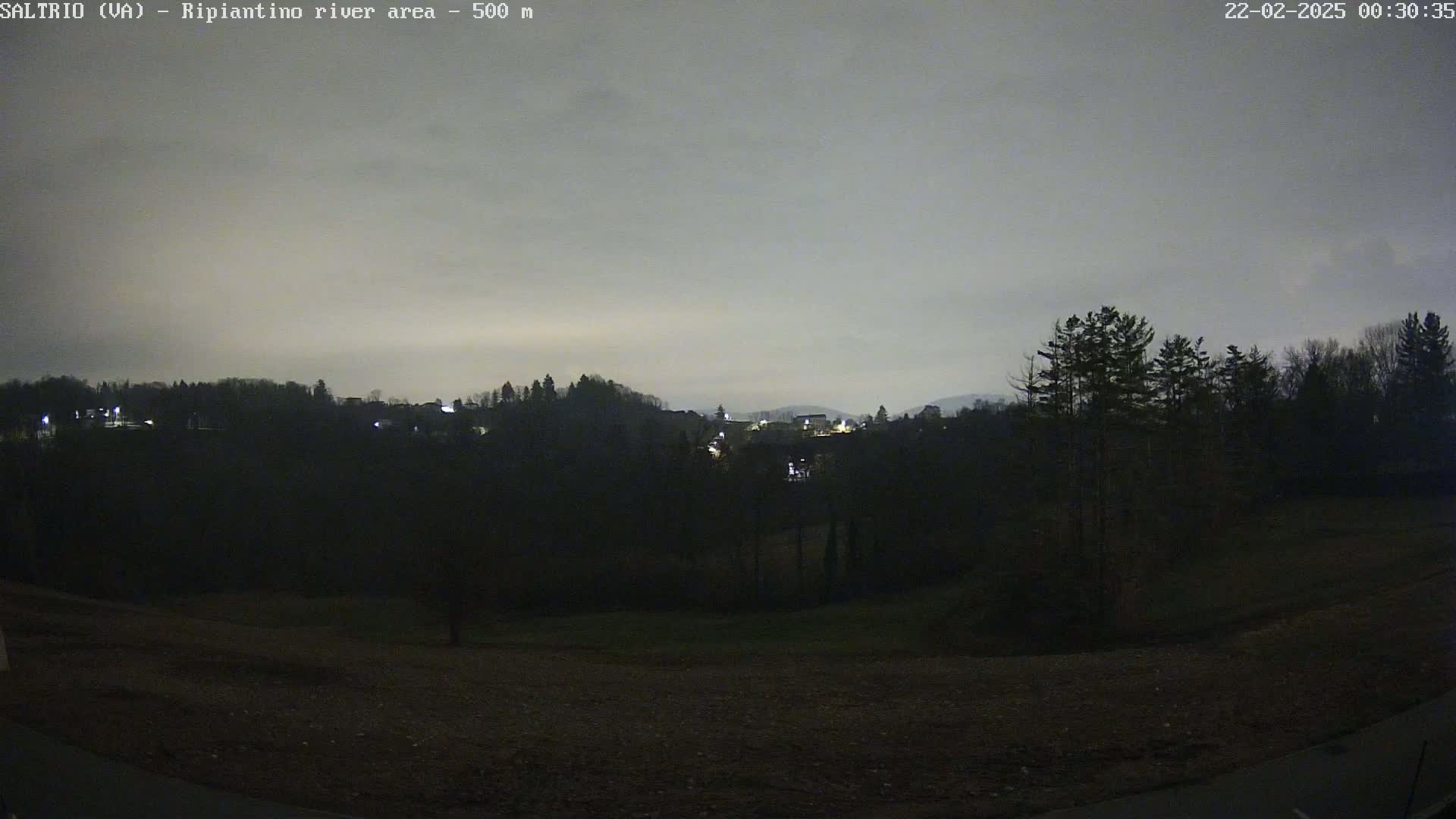 A nighttime view of a dimly lit town nestled among dark hills under an overcast sky.