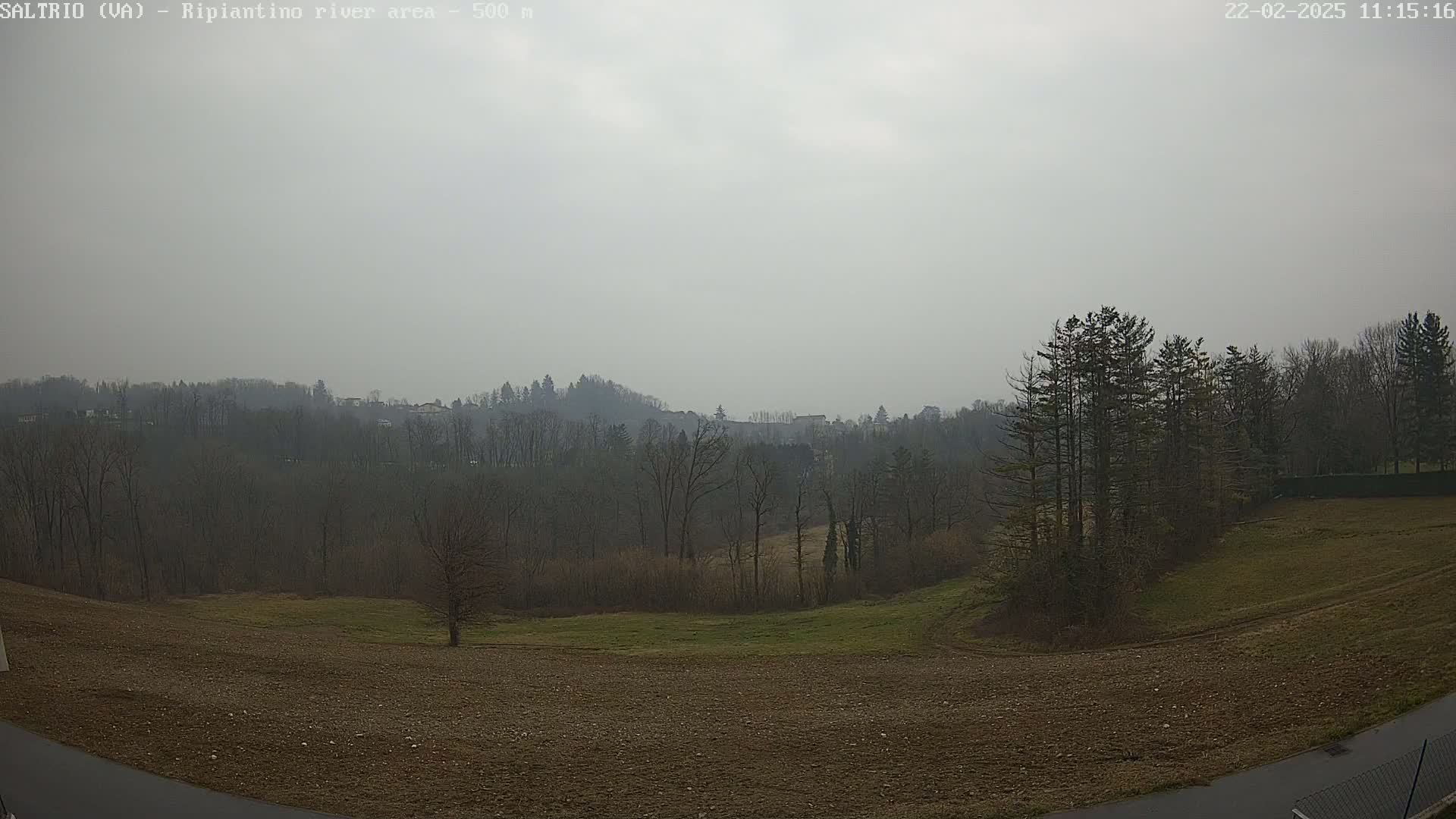 A hazy, overcast day reveals a landscape of plowed fields, sparse trees, and a distant wooded hillside.
