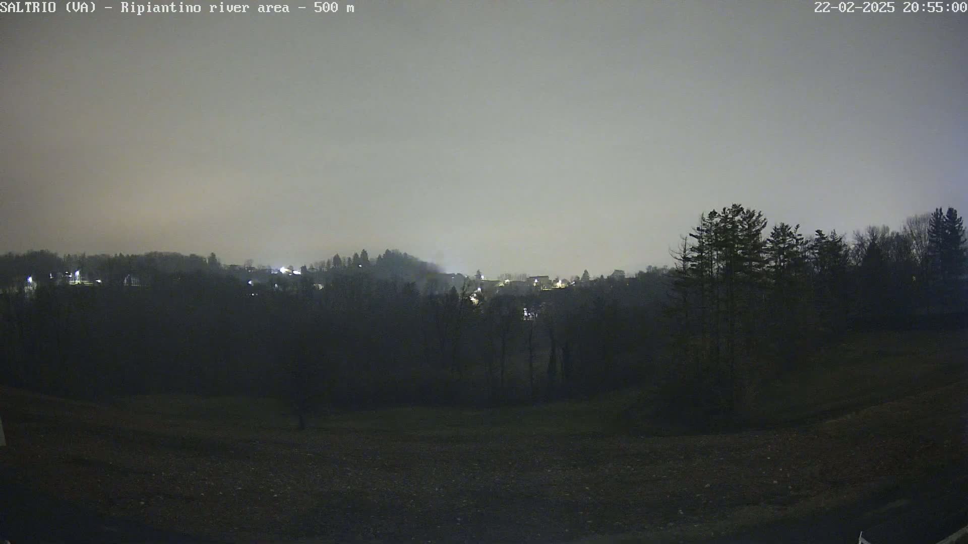 A nighttime view of a dimly lit town nestled among dark hills under a hazy sky.