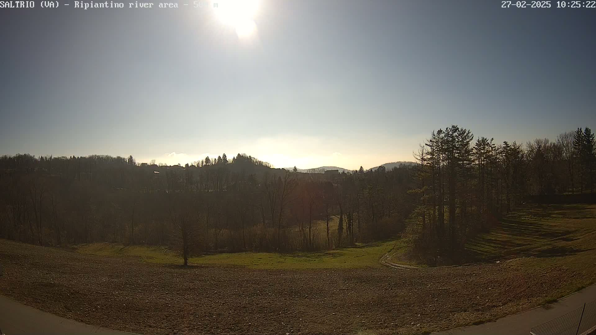 A sunny day reveals a plowed field in the foreground, overlooking a line of bare trees and hills in the distance.