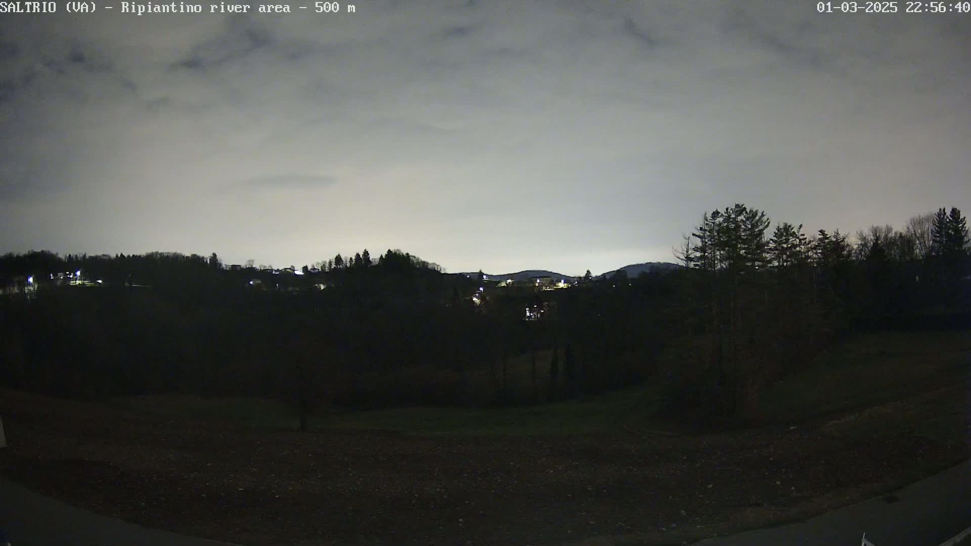 A nighttime view of dark, tree-covered hills under a cloudy, gray sky.