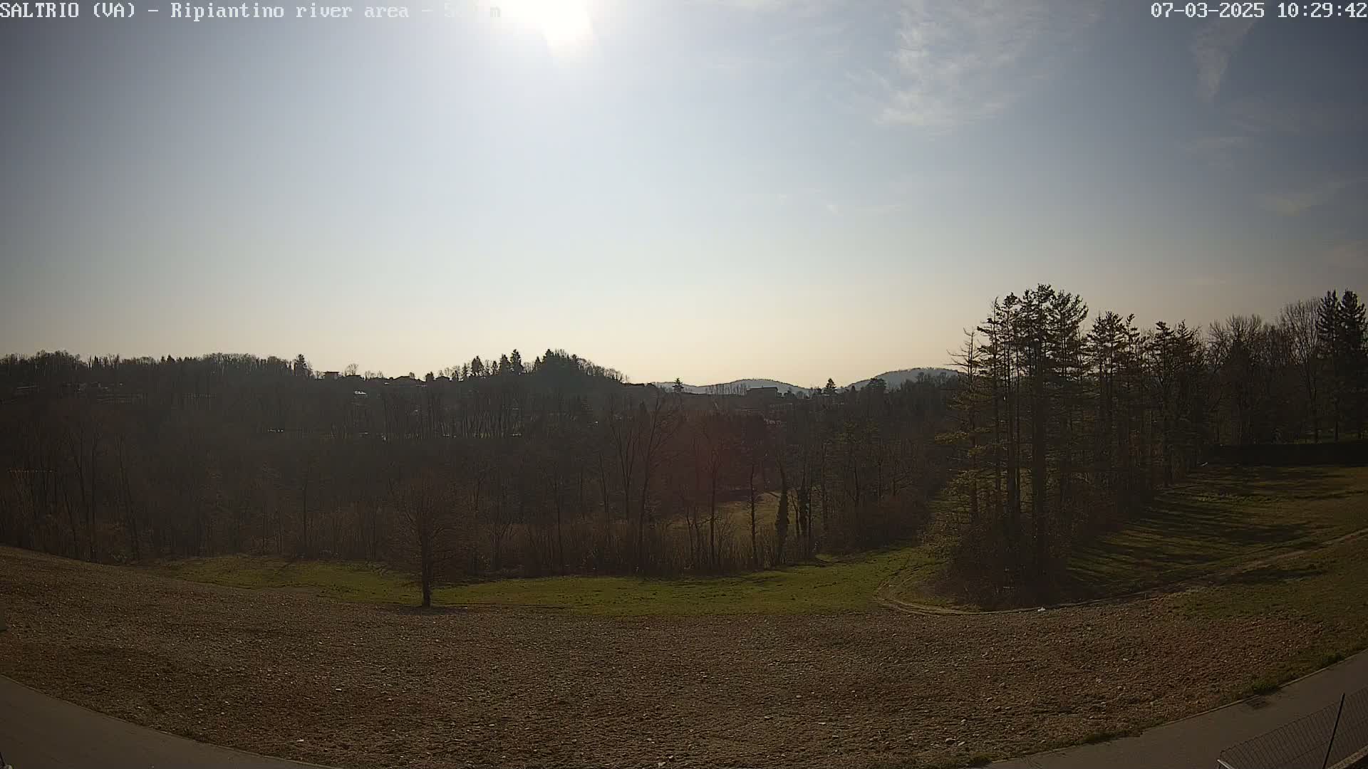 A mostly sunny day reveals a hilly landscape of dark green trees and brown fields, with a few buildings visible in the distance.