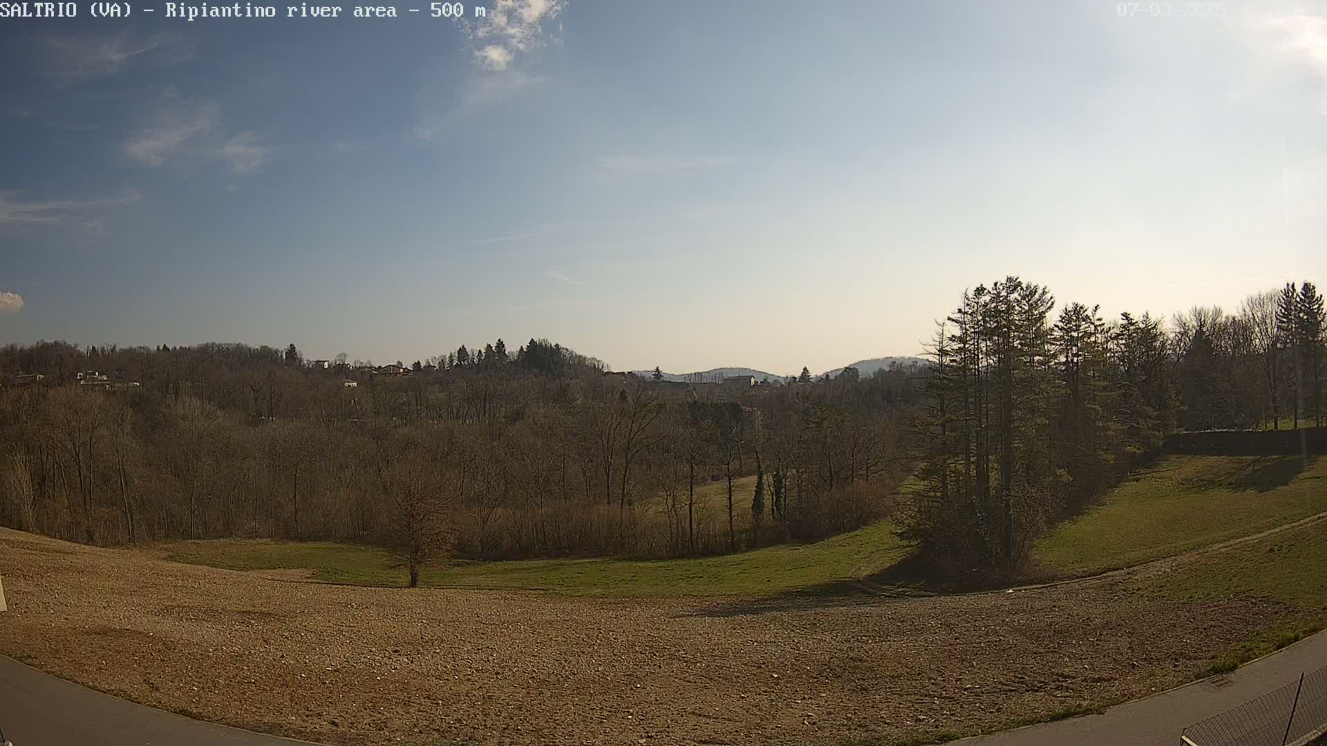 A mostly sunny day overlooks a plowed field, bare winter trees, and distant hills.