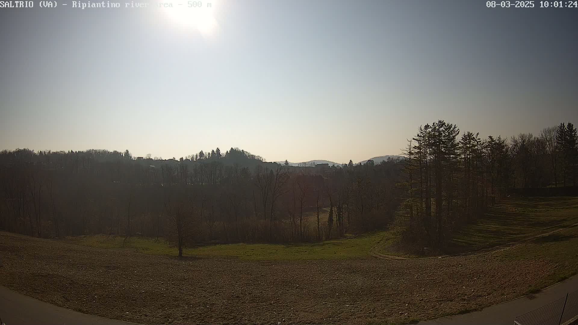 A sunny day reveals a hilly landscape with bare deciduous trees, patches of grass, and a plowed field in the foreground.