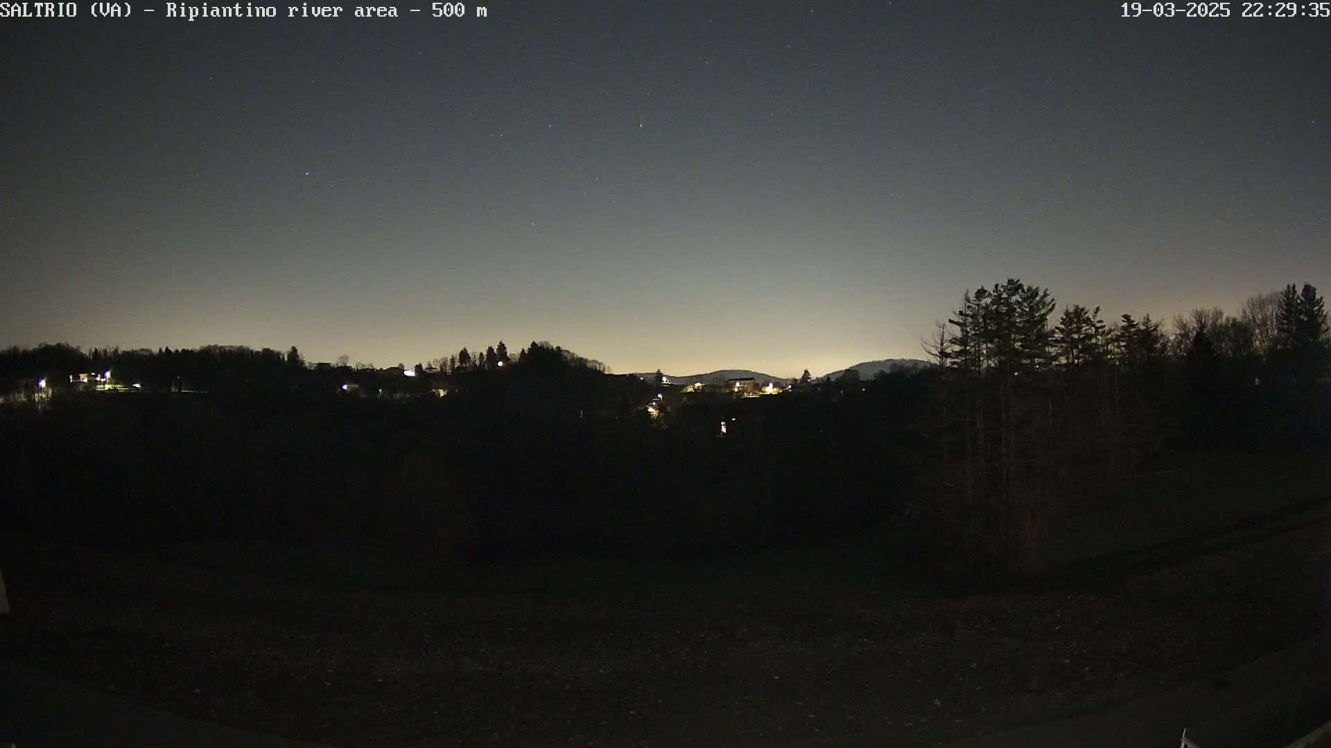 A nighttime view of a dark, silhouetted landscape with a few scattered lights, under a clear, starry sky.
