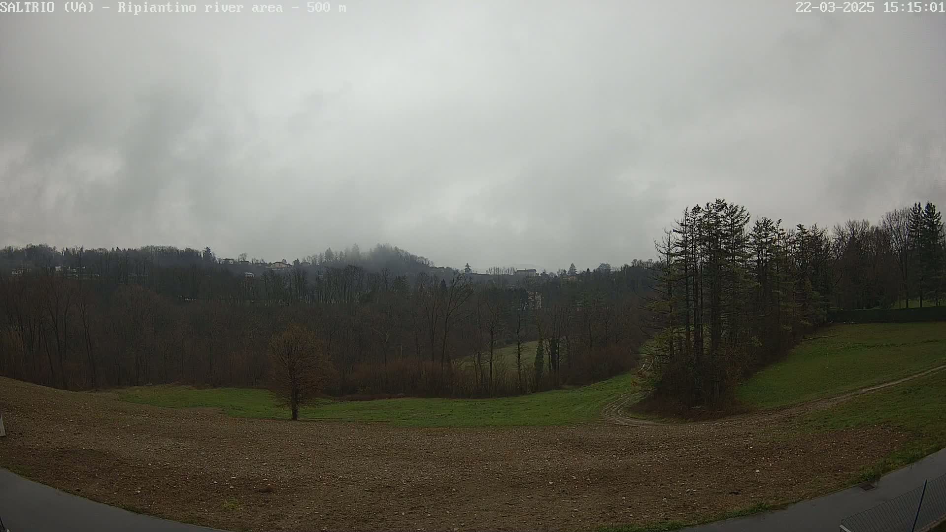 A mostly overcast sky hangs over a hilly landscape of bare trees and brown and green fields.