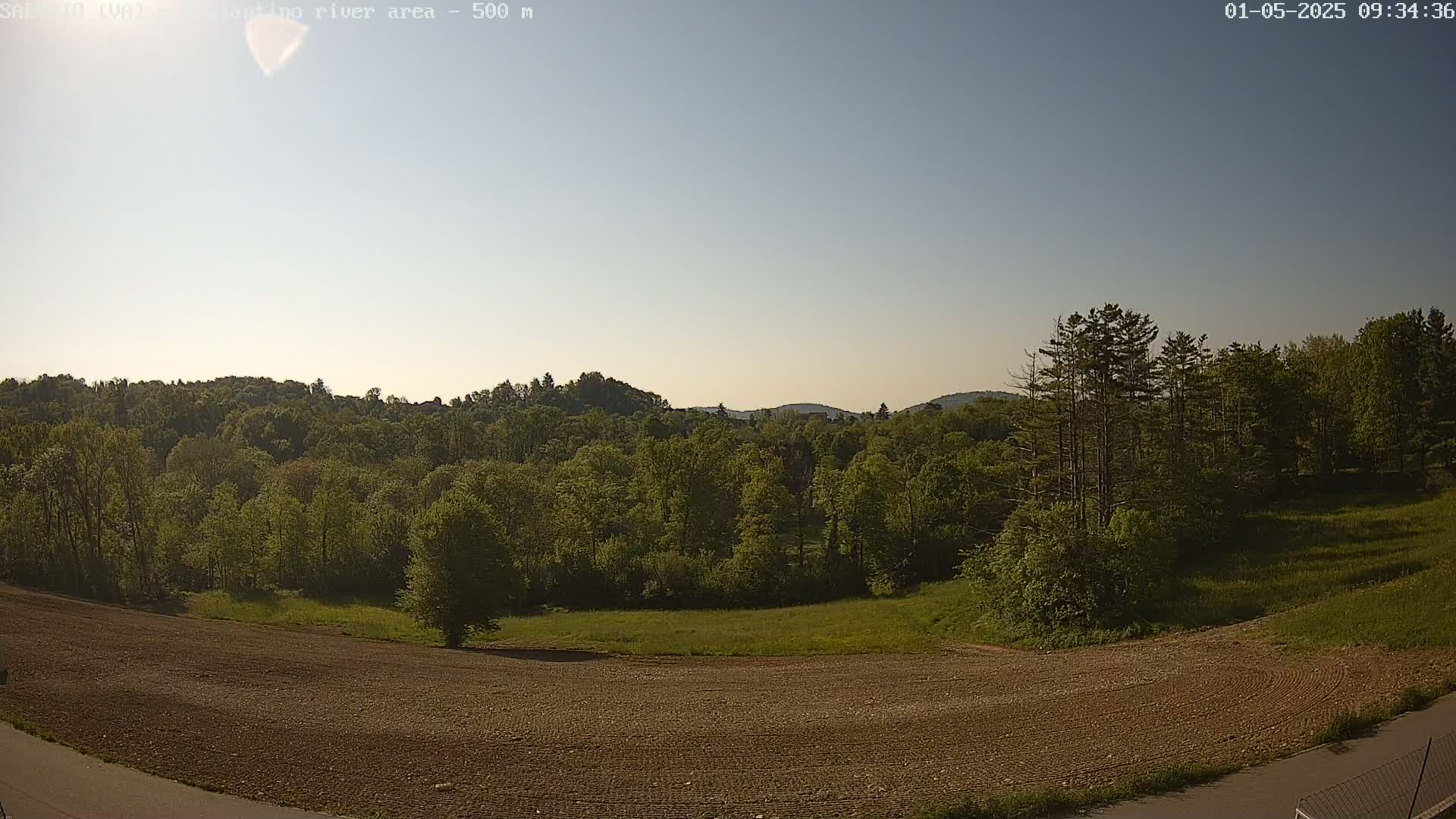 A plowed field and a line of trees sit before a large expanse of forest under a clear, sunny sky.