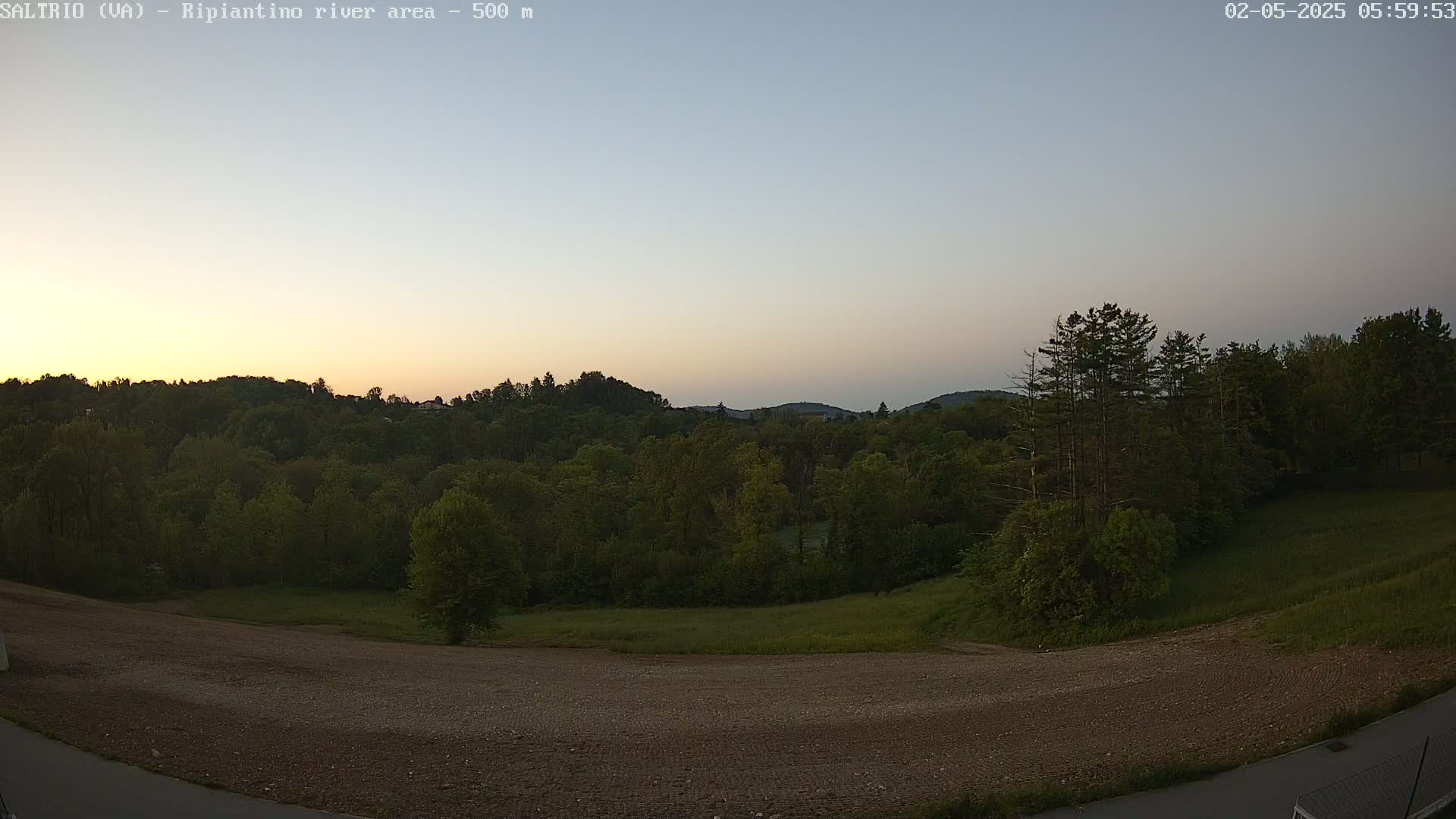 A tranquil sunset over a verdant landscape of trees and a barren, plowed field.