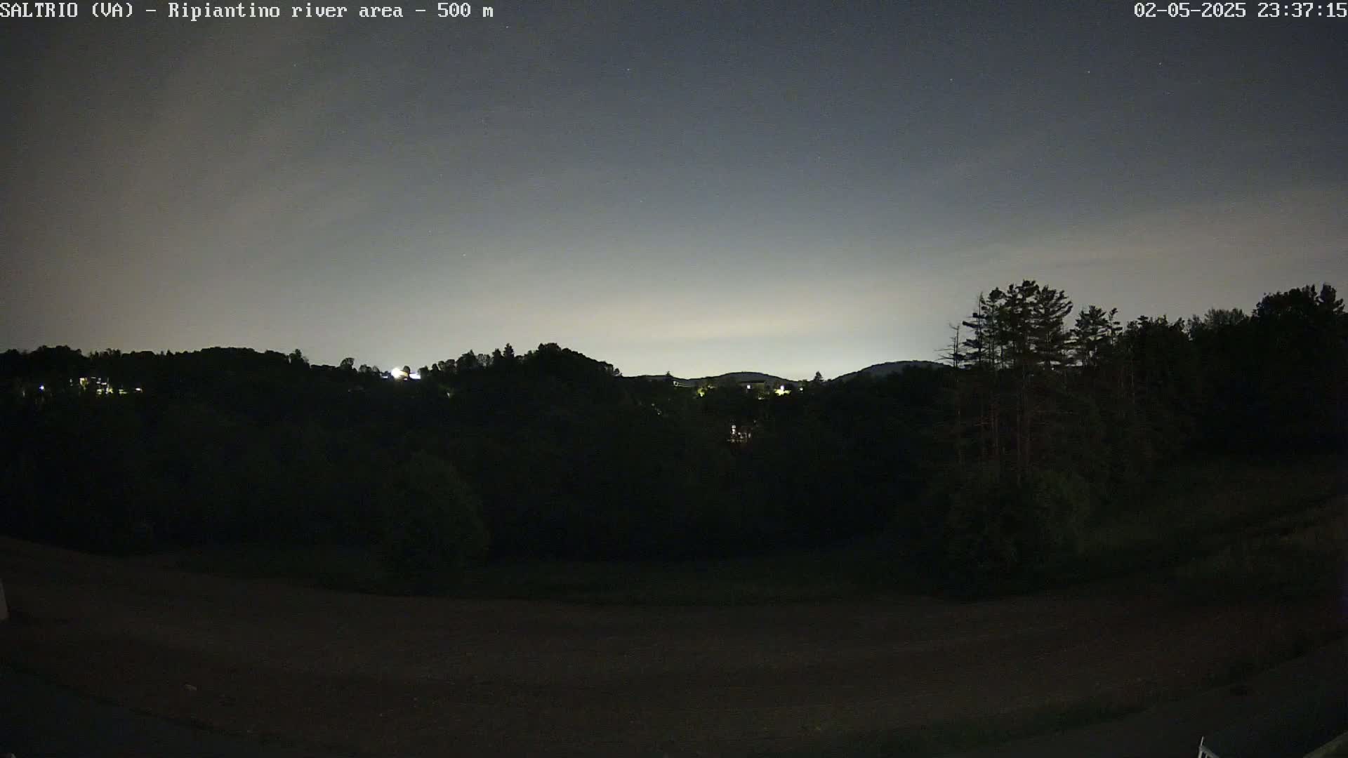A nighttime view of dark, tree-covered hills under a mostly clear, dark sky.