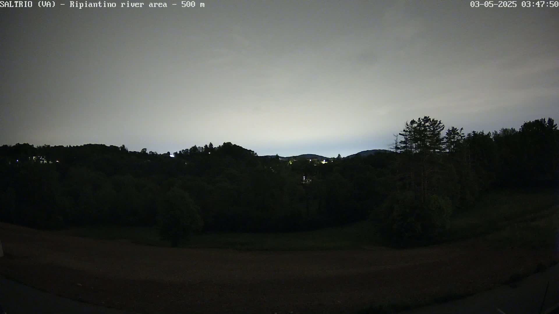 A nighttime view of dark, tree-covered hills under a mostly cloudy, light gray sky.